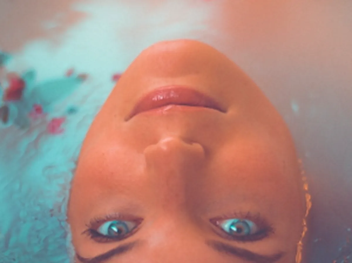 Woman with glowing skin floating in water with flower petals